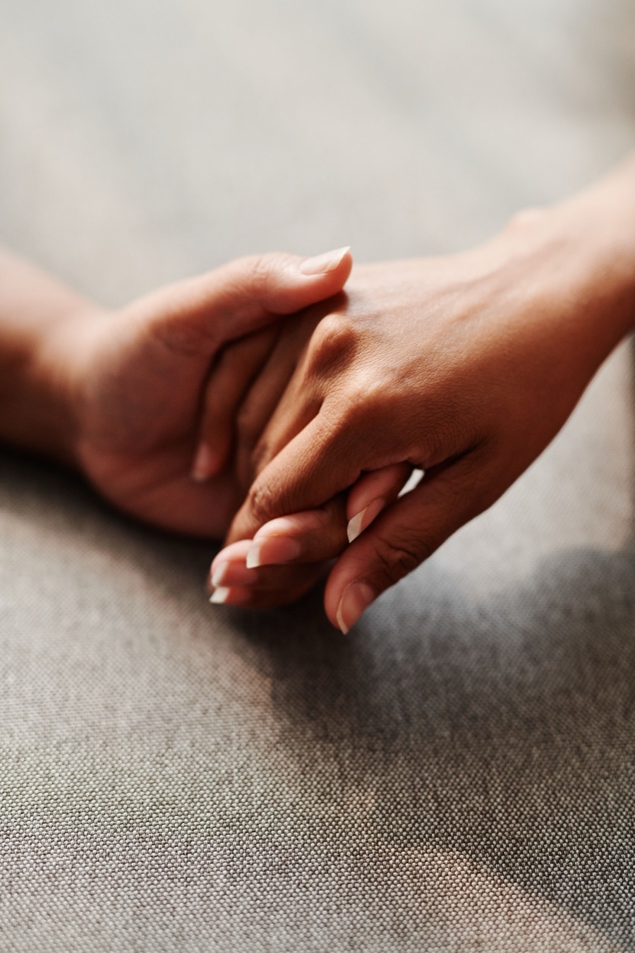 Two people holding hands, resting on a grey fabric sofa